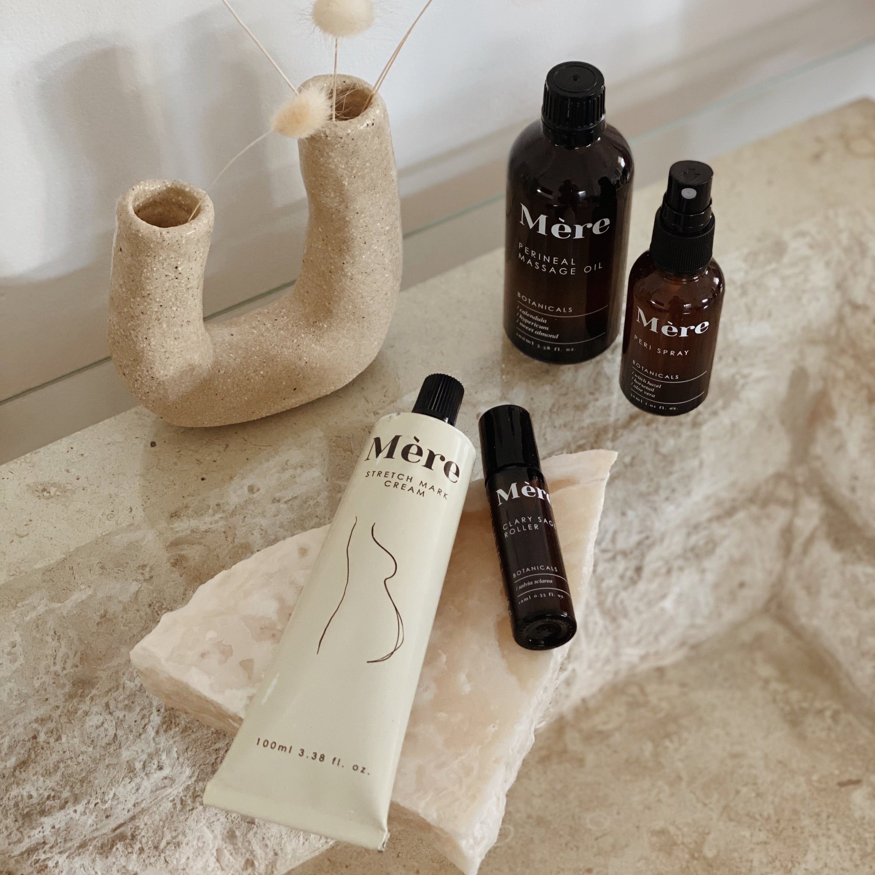 Show multiple mere botanicals products displayed on piece of stone with aesthetic vase on stone coffee table