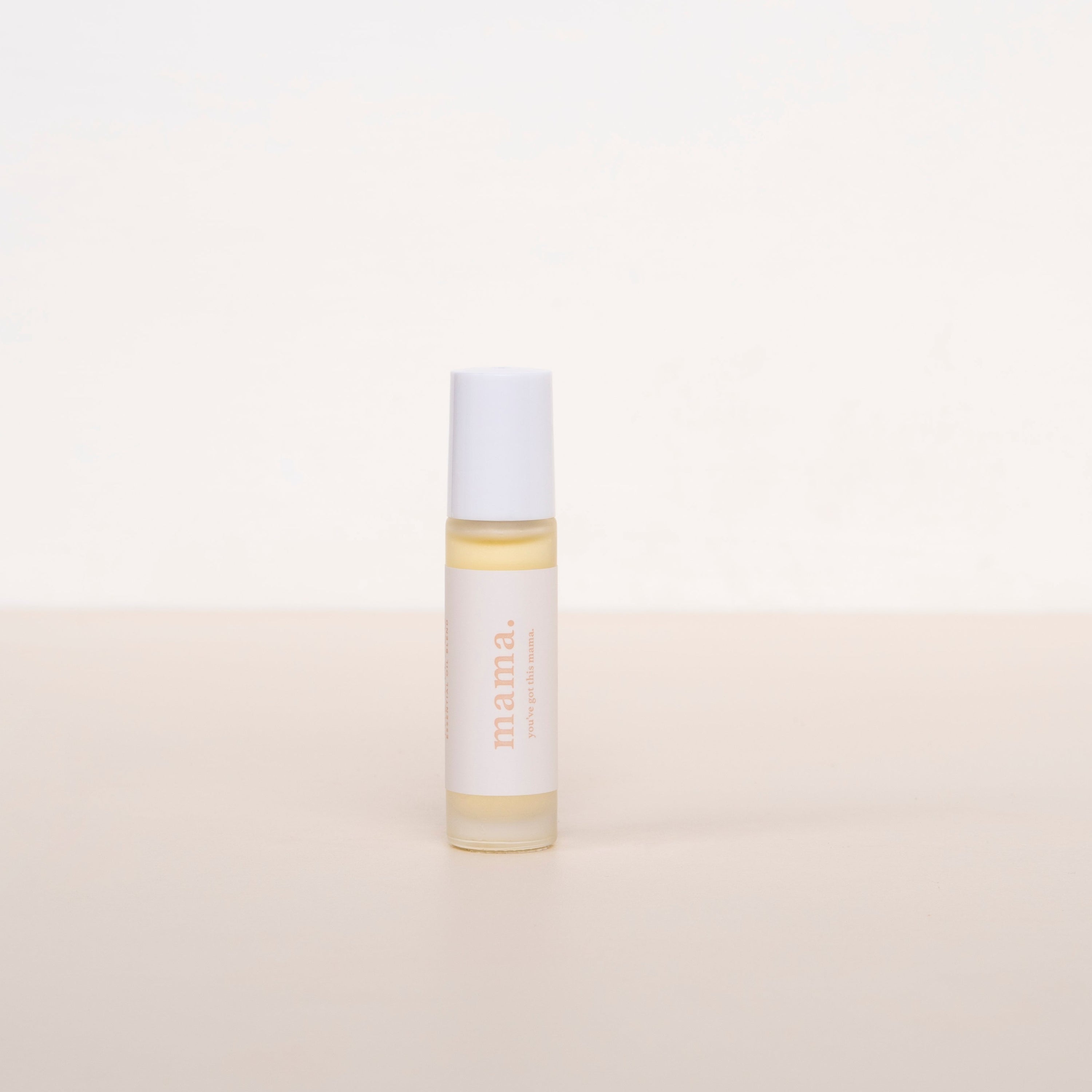 Cle naturals Mama essential oil roller blend standing upright against neutral background, small glass cannister with white label and white lid, orange text
