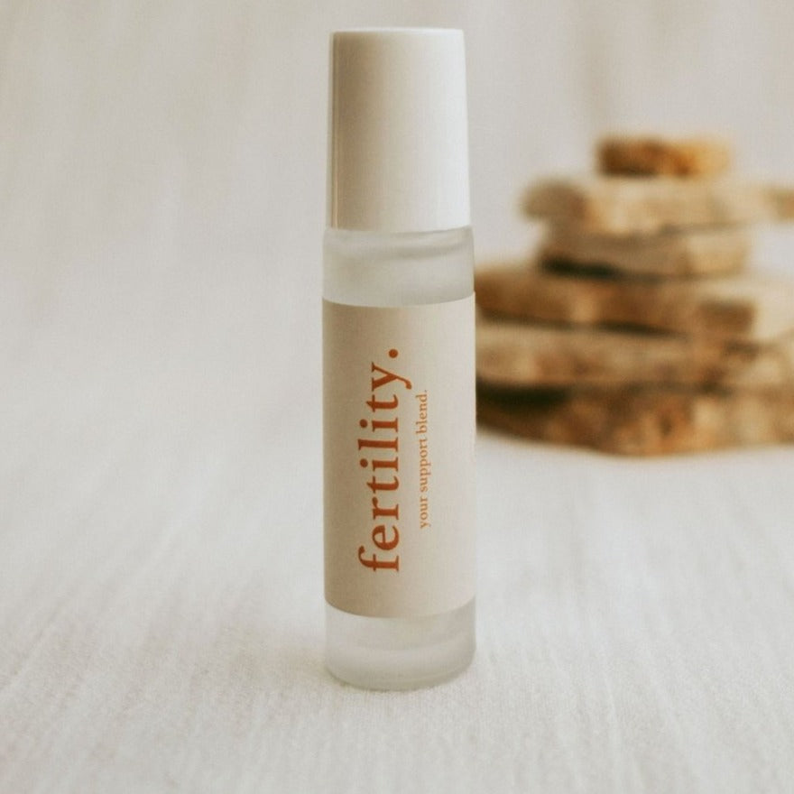 Close up cle naturals fertility essential oil roller, pieces os stone stacked in the background of shot