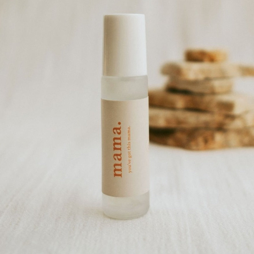 Cle naturals mama essential oil roller standing infront of stone oieces stacked on top of one another