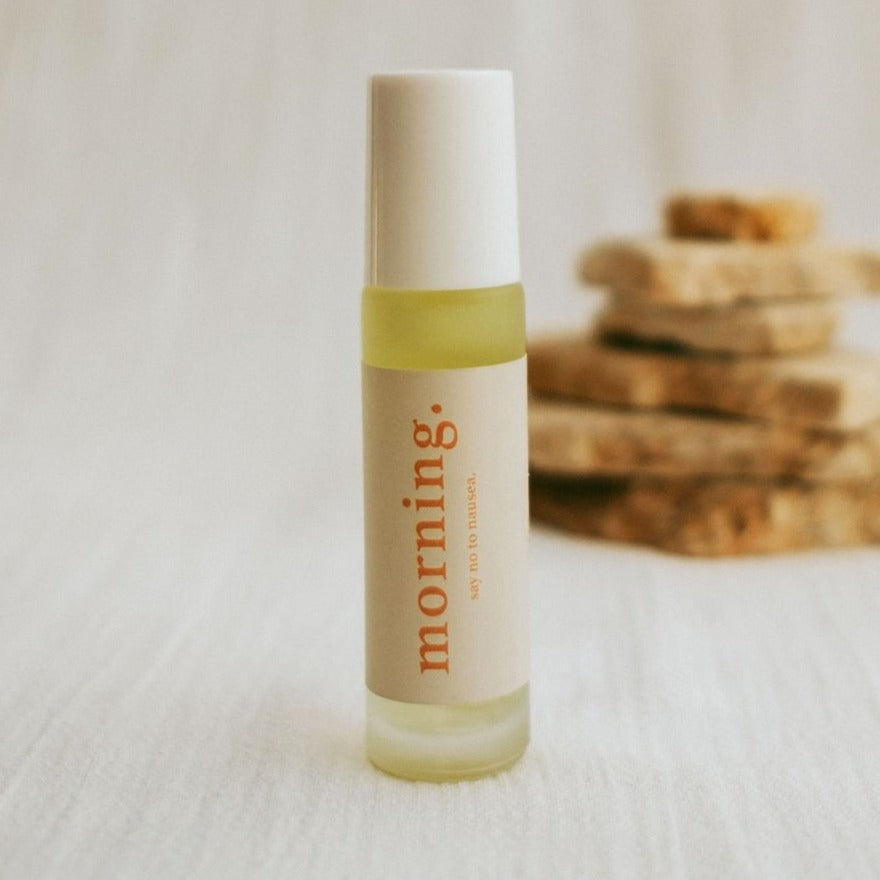 Close up of cle naturals morning essential oil roller blend standing up right wth pieces of stone stacked in background